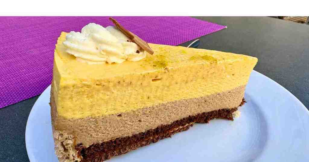 A slice of layered traditional German mango cream cake with chocolate and vanilla mousse on a white plate, served at a cafe in Ulm, Germany.