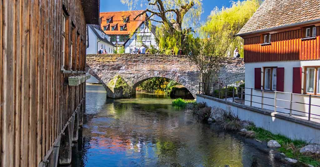 A scenic view of a historic stone bridge crossing the Blau river, surrounded by traditional half-timbered houses in the Fischerviertel district of Ulm, Germany.