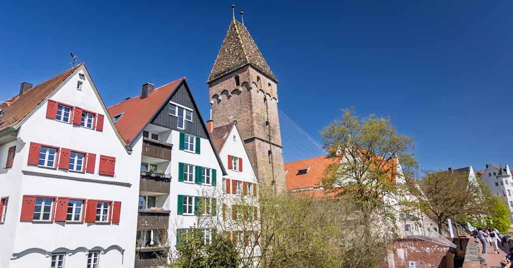 The historic leaning Metzgerturm (Butcher's Tower) built into the medieval city walls of Ulm, Germany, set against a clear blue sky.