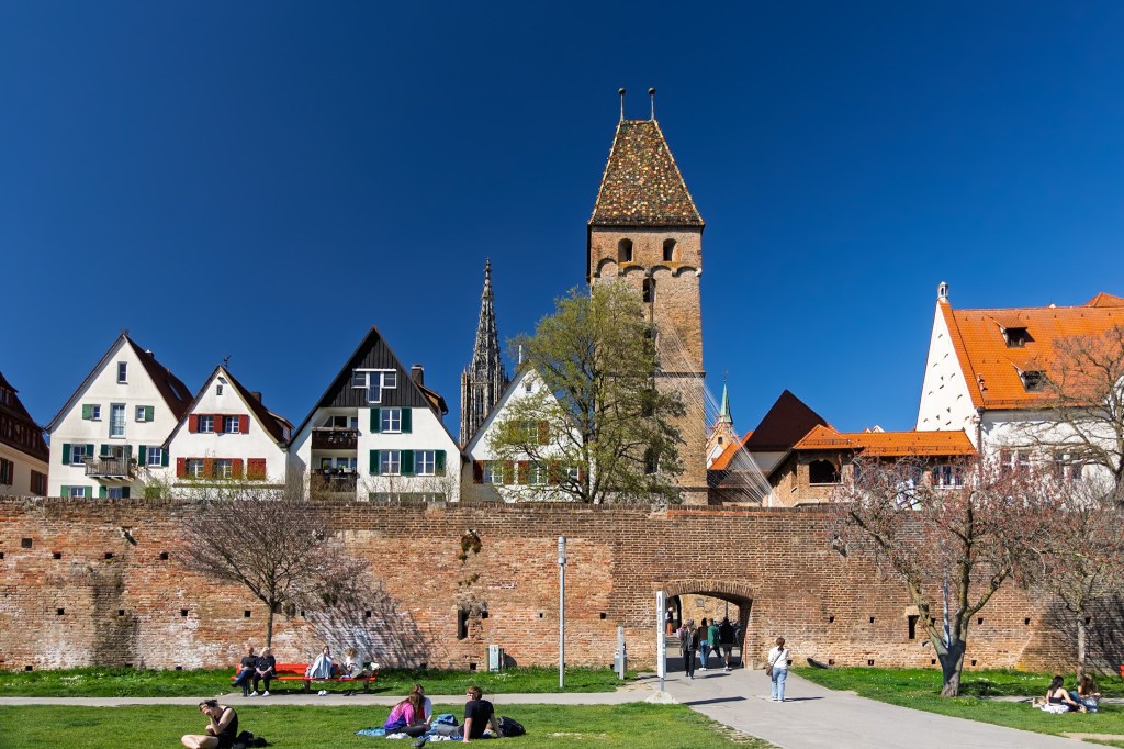 The leaning Metzgerturm tower and medieval city gate leading to the sunny Danube river promenade in Ulm, Germany.